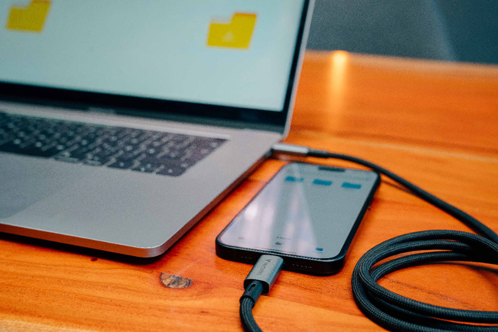 Laptop and smartphone on a wooden surface with a cable connecting them.